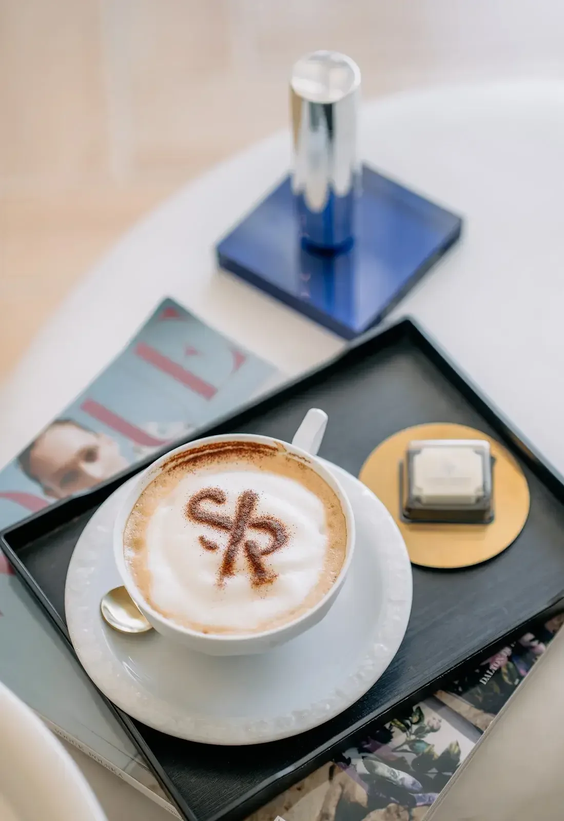 Kawa latte z logotypem SP odbitym w piance, na czarnym talerzyku ze złotą łyżeczką